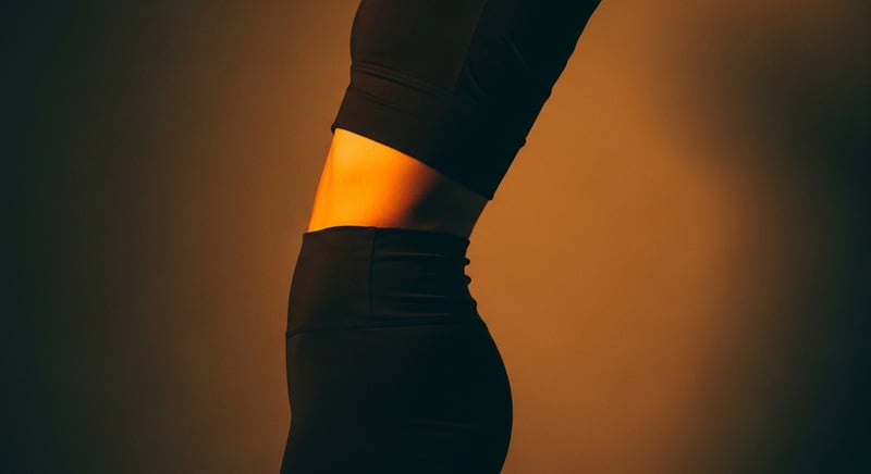 Editorial side-profile photograph of a standing person whose lower ribs jut forward and up, low back arched, face cropped above the nose