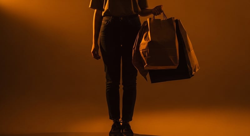 Editorial photograph of a person carrying a heavy bag in one hand with the loaded hip dropped and the torso leaning away, showing the pelvis unlocked and the spine side-bending, warm amber light, no identifiable face